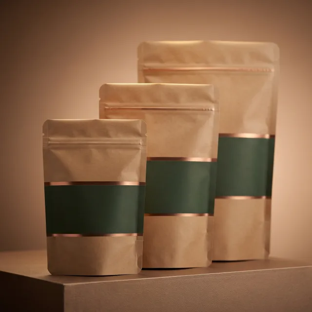 Three kraft stand-up pouches in graduated sizes on a pale plinth, each banded in forest green between two copper foil rules, lit warm against a tan studio backdrop